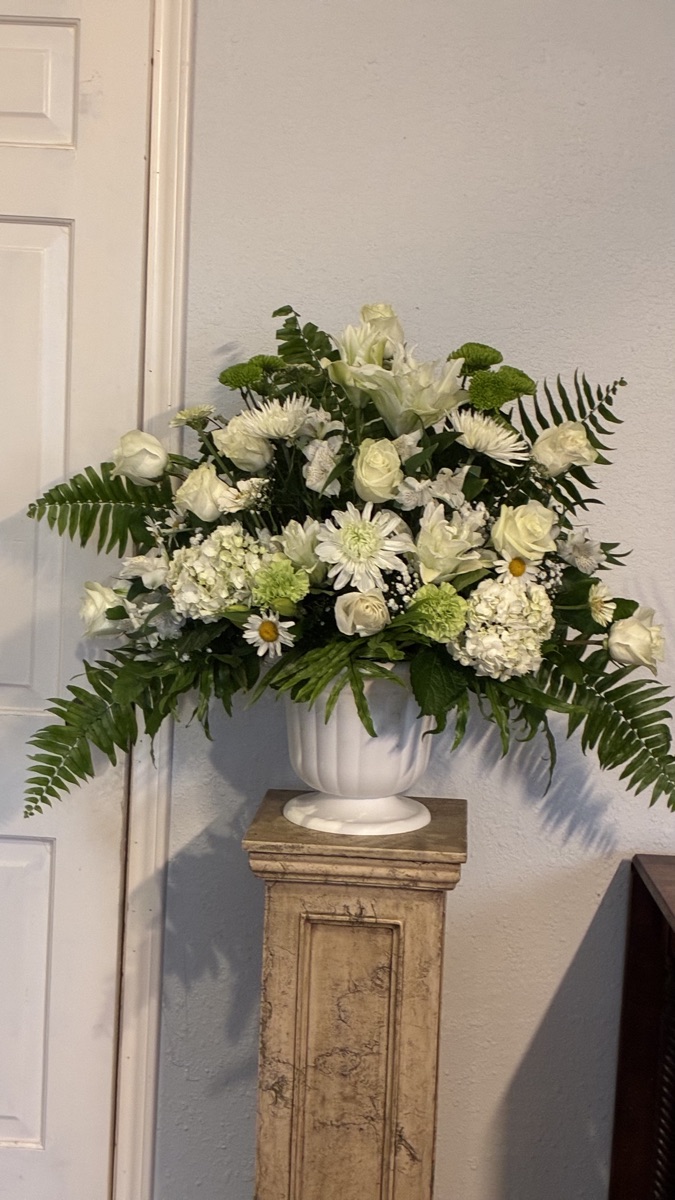 An all-white arrangement of lilies, hydrangea and daisies in a classic urn